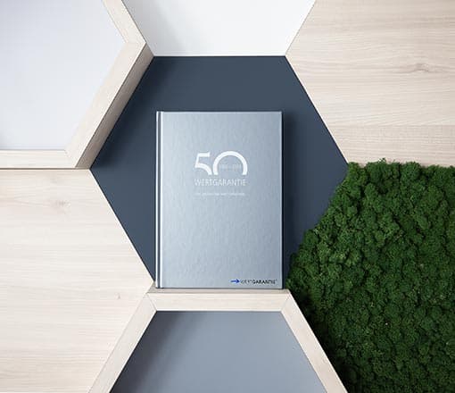 Ein Buch mit dem Titel 50 Jahre WERTGARANTIE Group steht in einem Warbenregal.