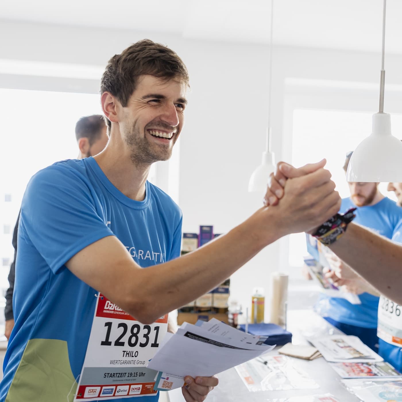 Ein Mitarbeiter im Laufshirt mit Startnummer gibt einer anderen Person einen Handschlag