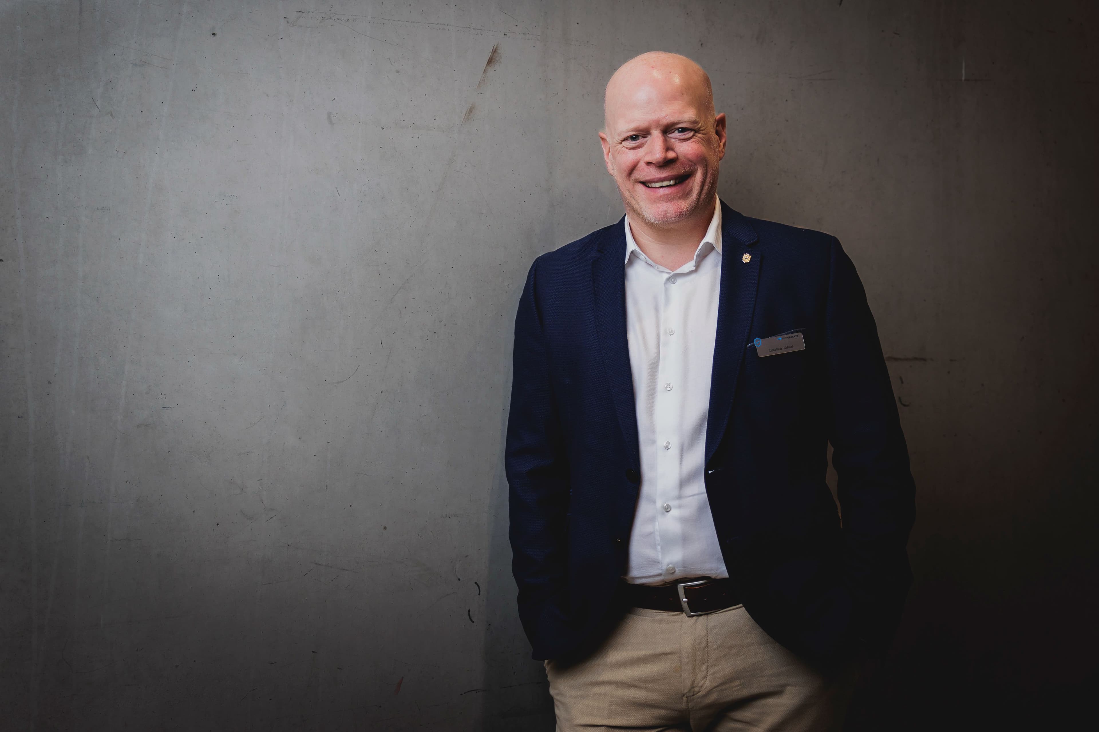 Der Vertriebsaußendienst Leiter Maurice Joehler steht im Anzug vor einer dunklen Wand.