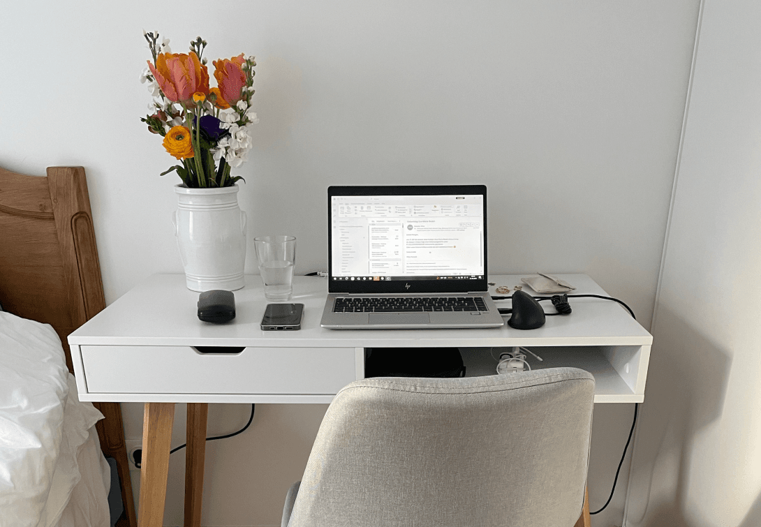 Der Arbeitsplatz von Karina, bestehend aus einem kleinem Tisch, einem Stuhl, dem aufgeklappten Laptop und einem Strauß Blumen.