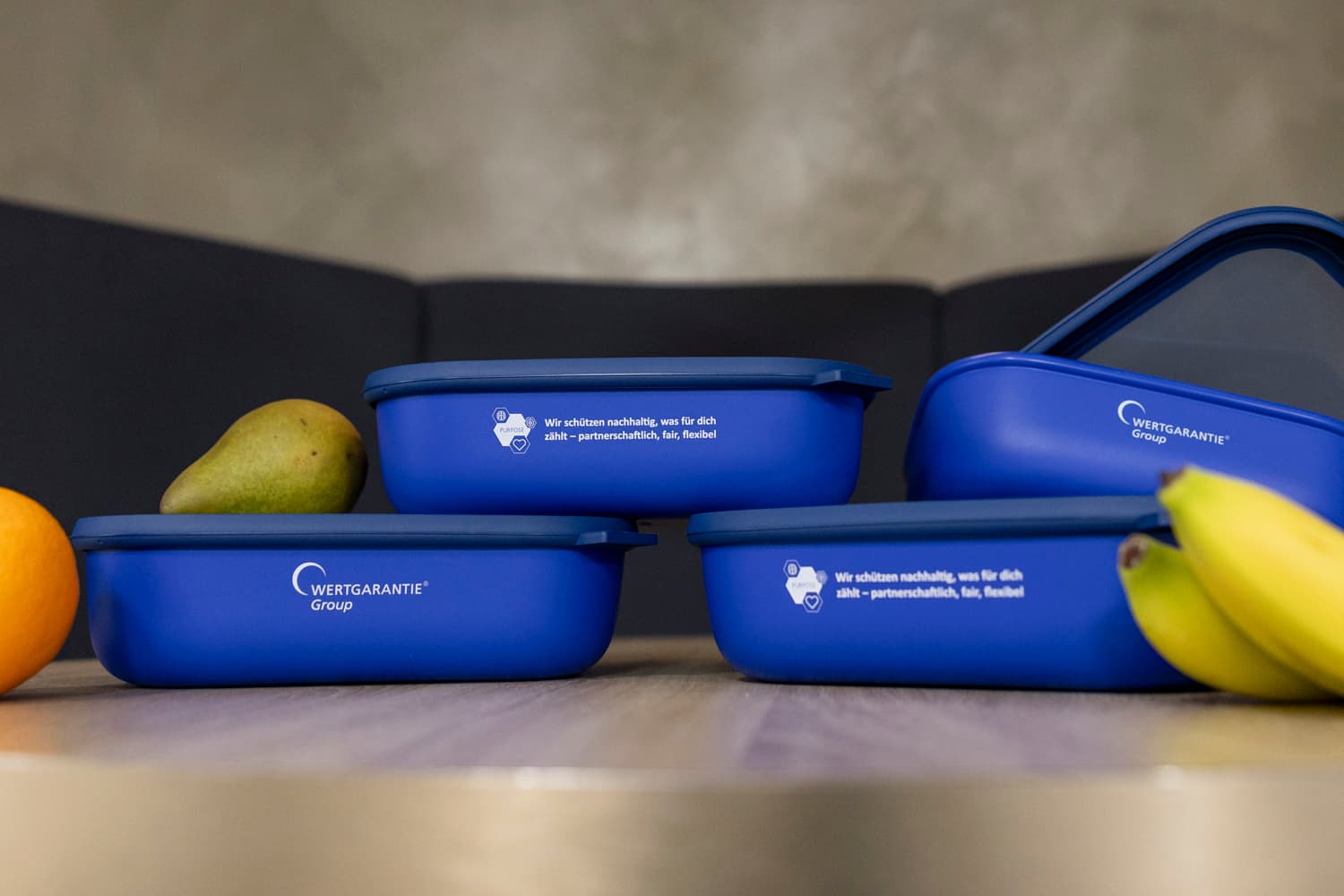 Vier blaue Mepal Aufbewahrungsdosen sind auf einem Tisch zu einem Turm aufgebaut. Daneben liegt Obst.