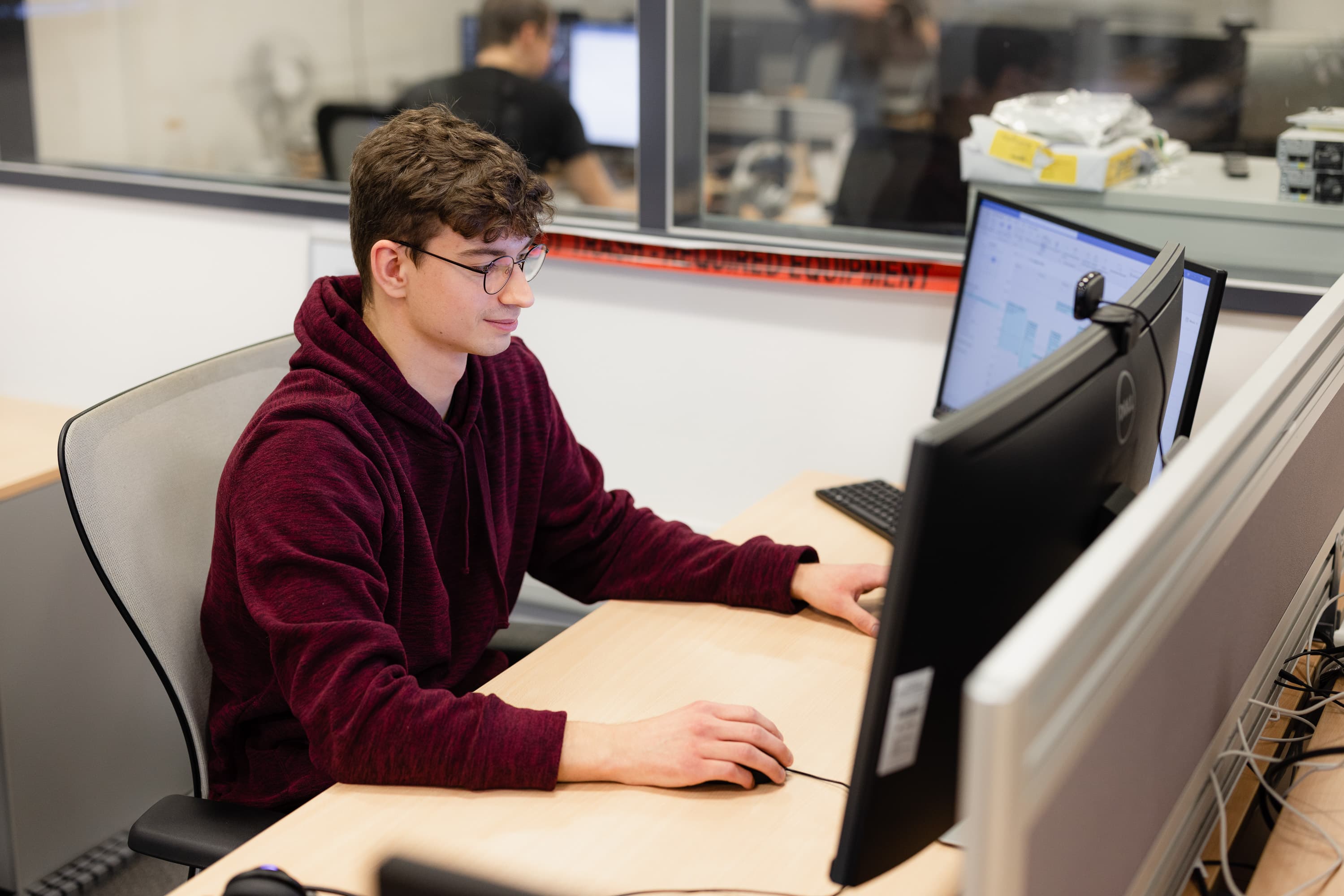 Ein junger IT-Mitarbeiter sitzt vor zwei Bildschirmen