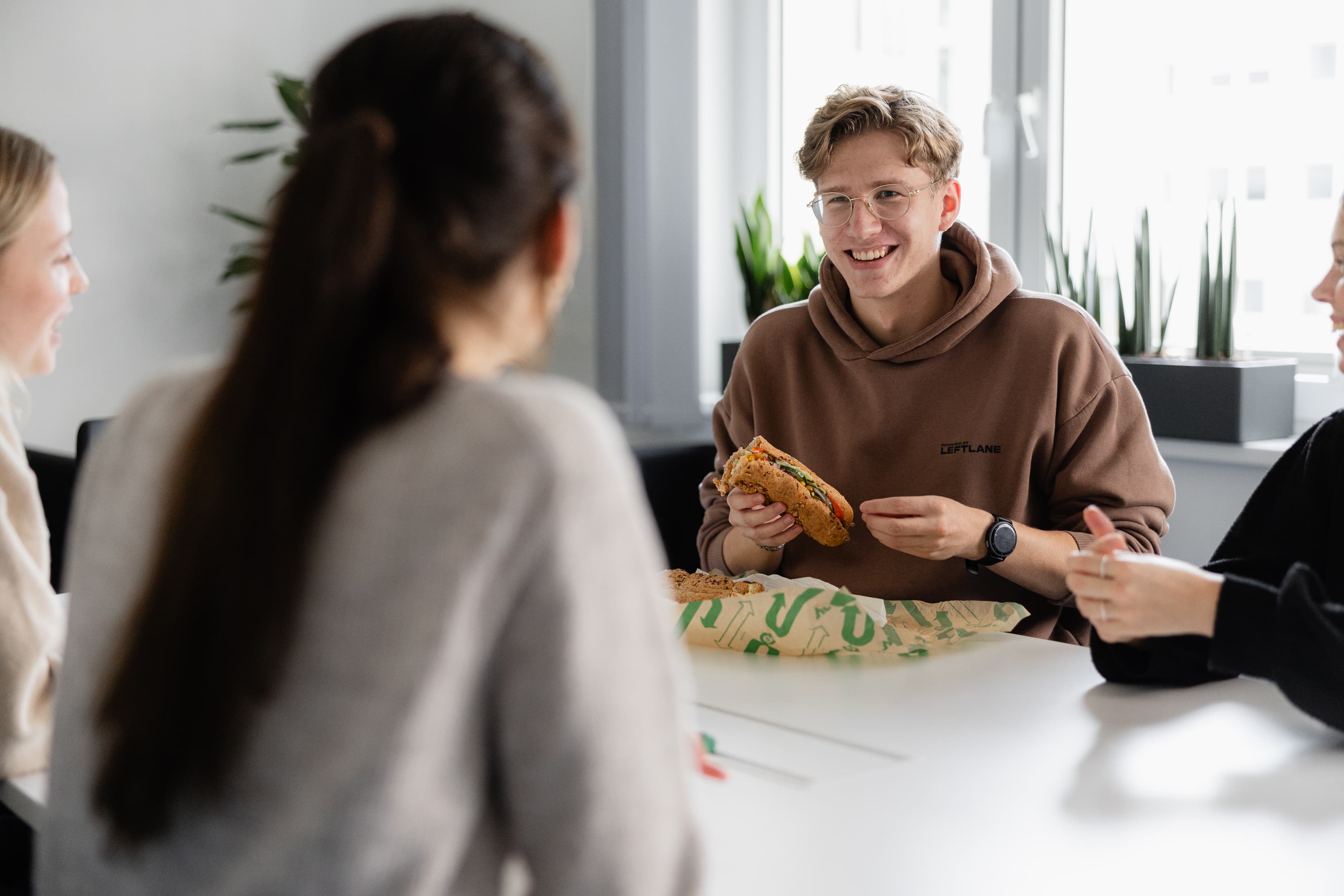 Unser Dualer Student Marcel Anker sitzt in der Mittagspause am Tisch und isst ein Baguette.
