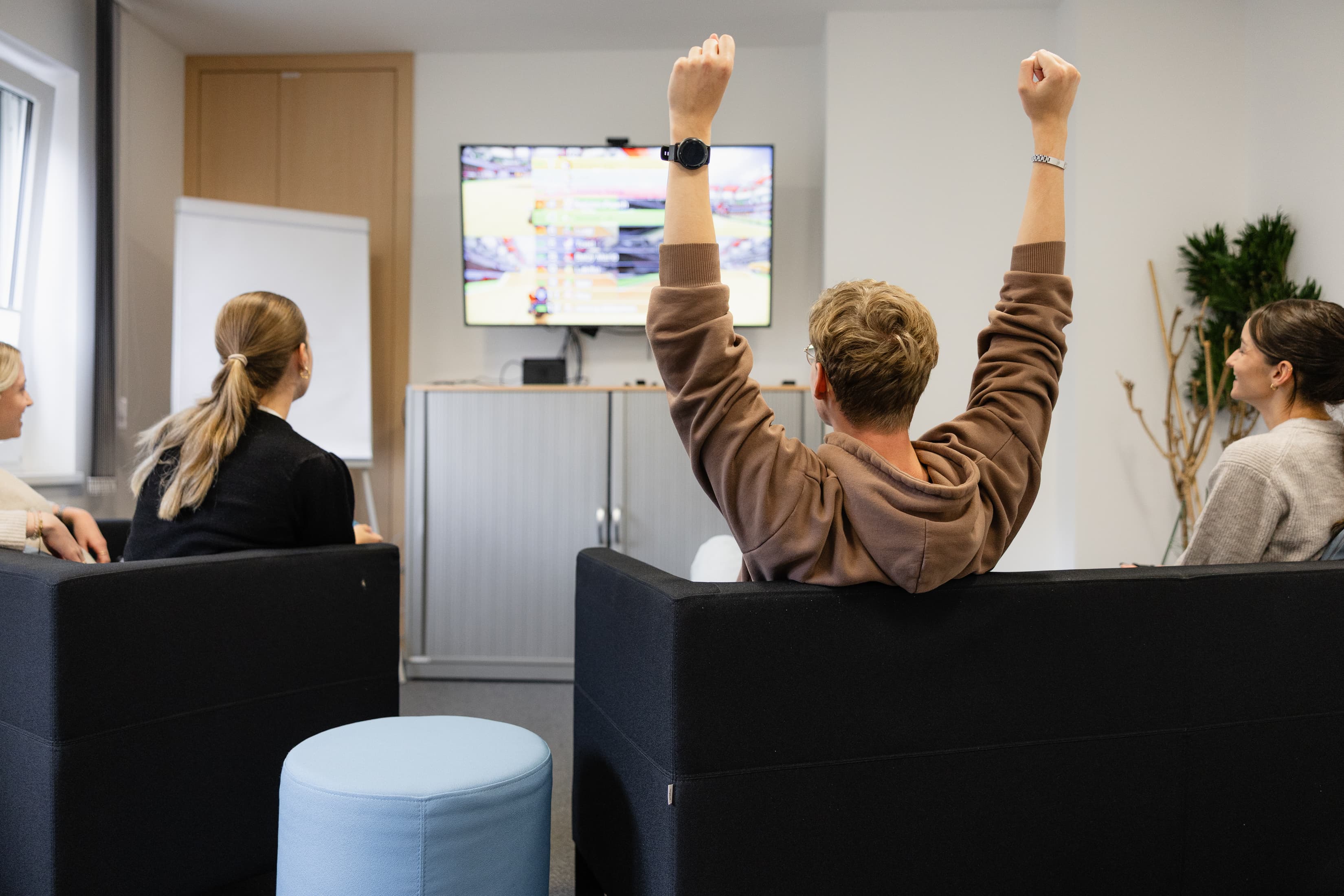 Unser Dualer Student Marcel Anker sitzt mit zwei Kolleginnen auf einem Sofa und zockt Mario Kart auf dem Fernseher.