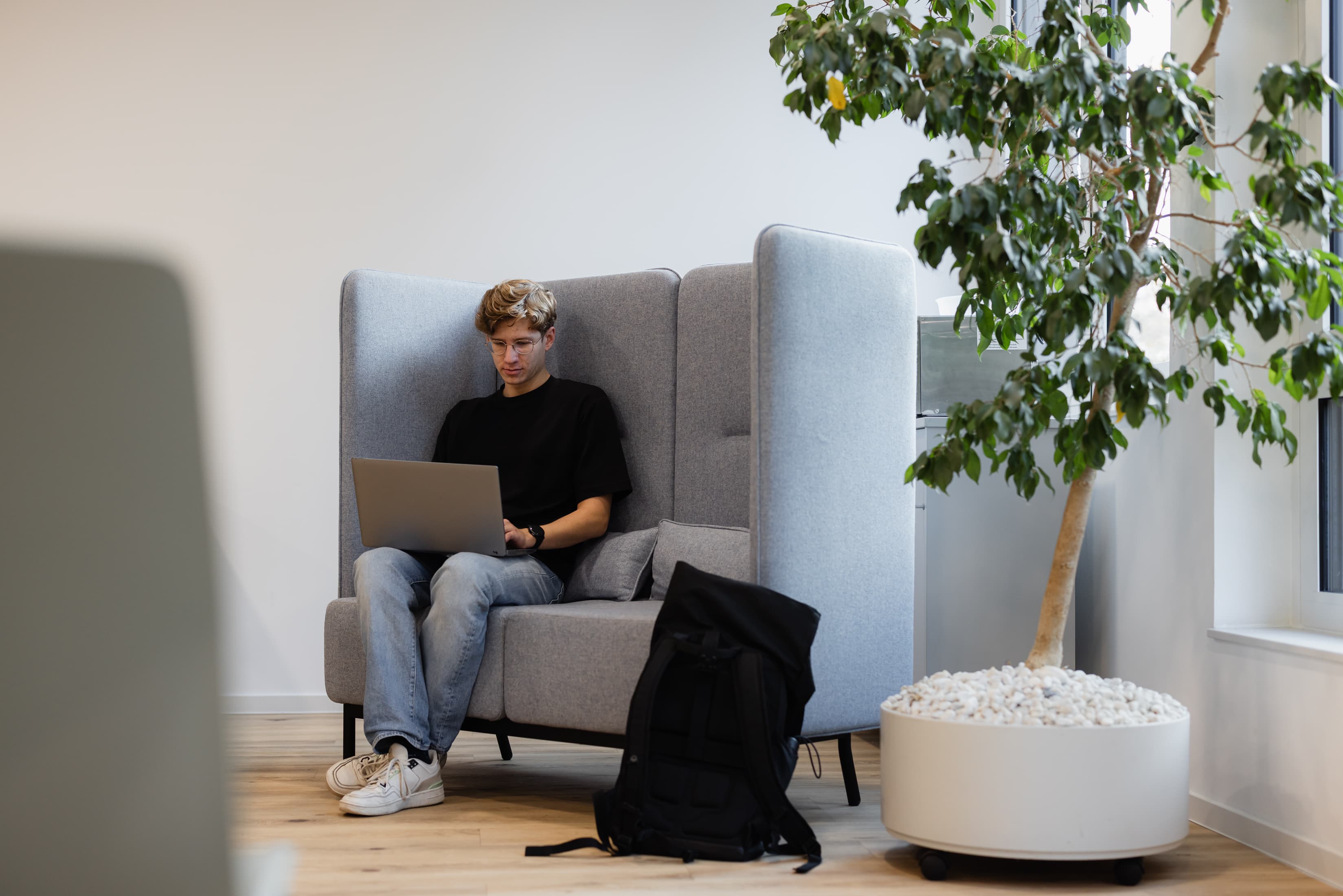 Unser Dualer Student Marcel Anker sitzt in der FHDW in einer Sofaecke und schaut auf seinen Laptop.