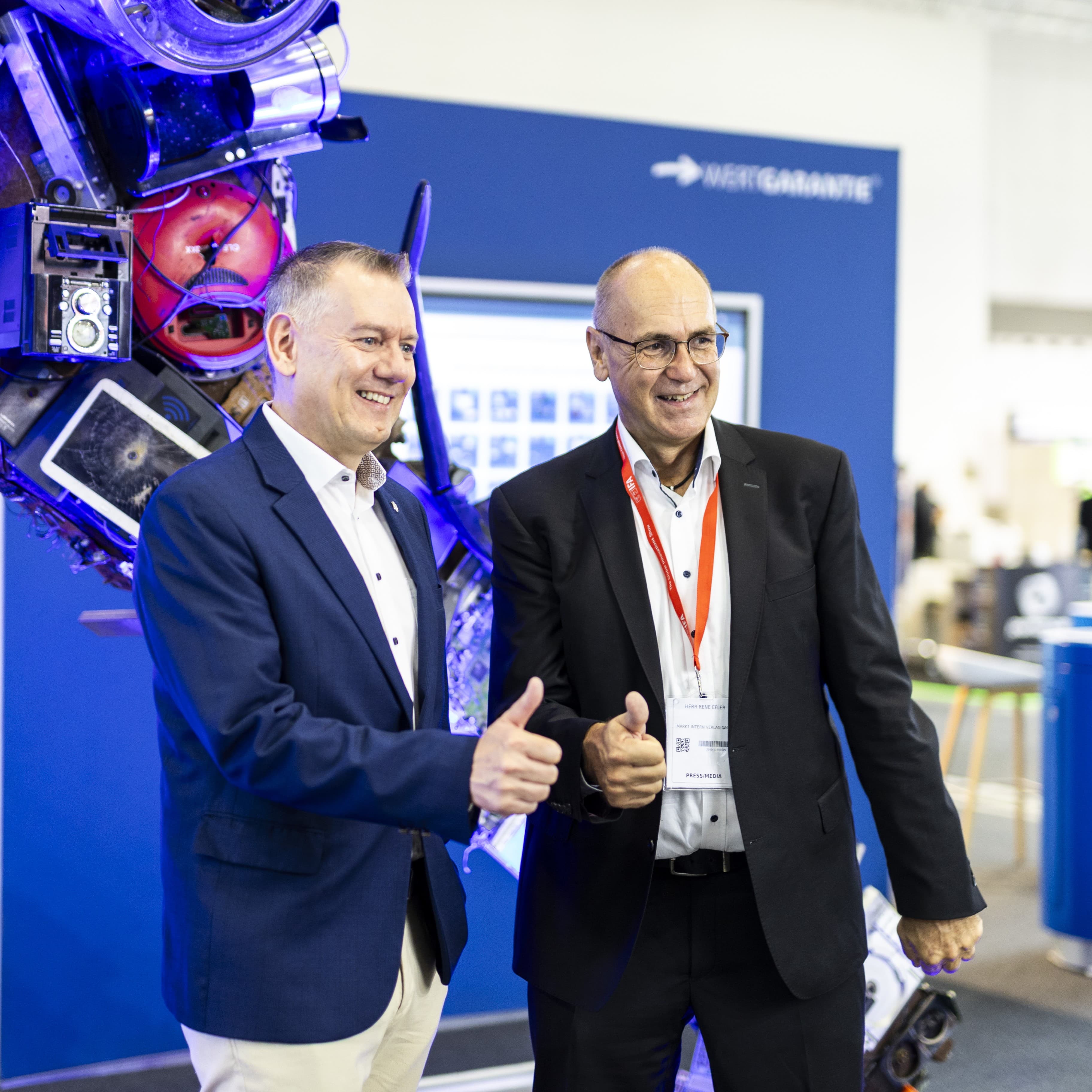 Zwei Männer stehen wir einem WERTGARANTIE-Messestand und halten einen Daumen hoch