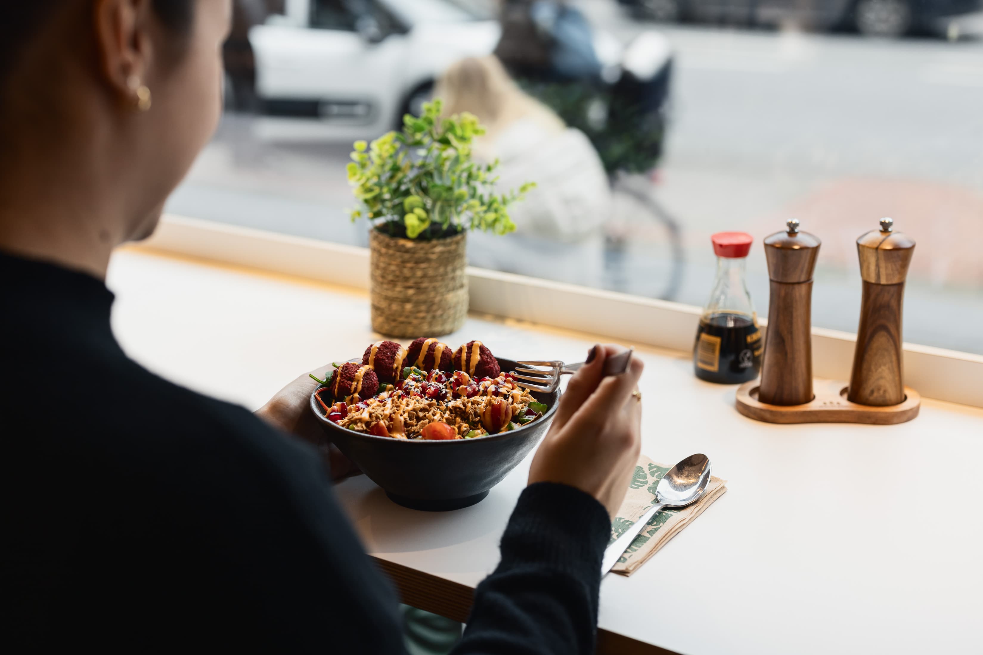 Eine Person sitzt an einem Tisch im Fenster und isst ein Mittagessen.
