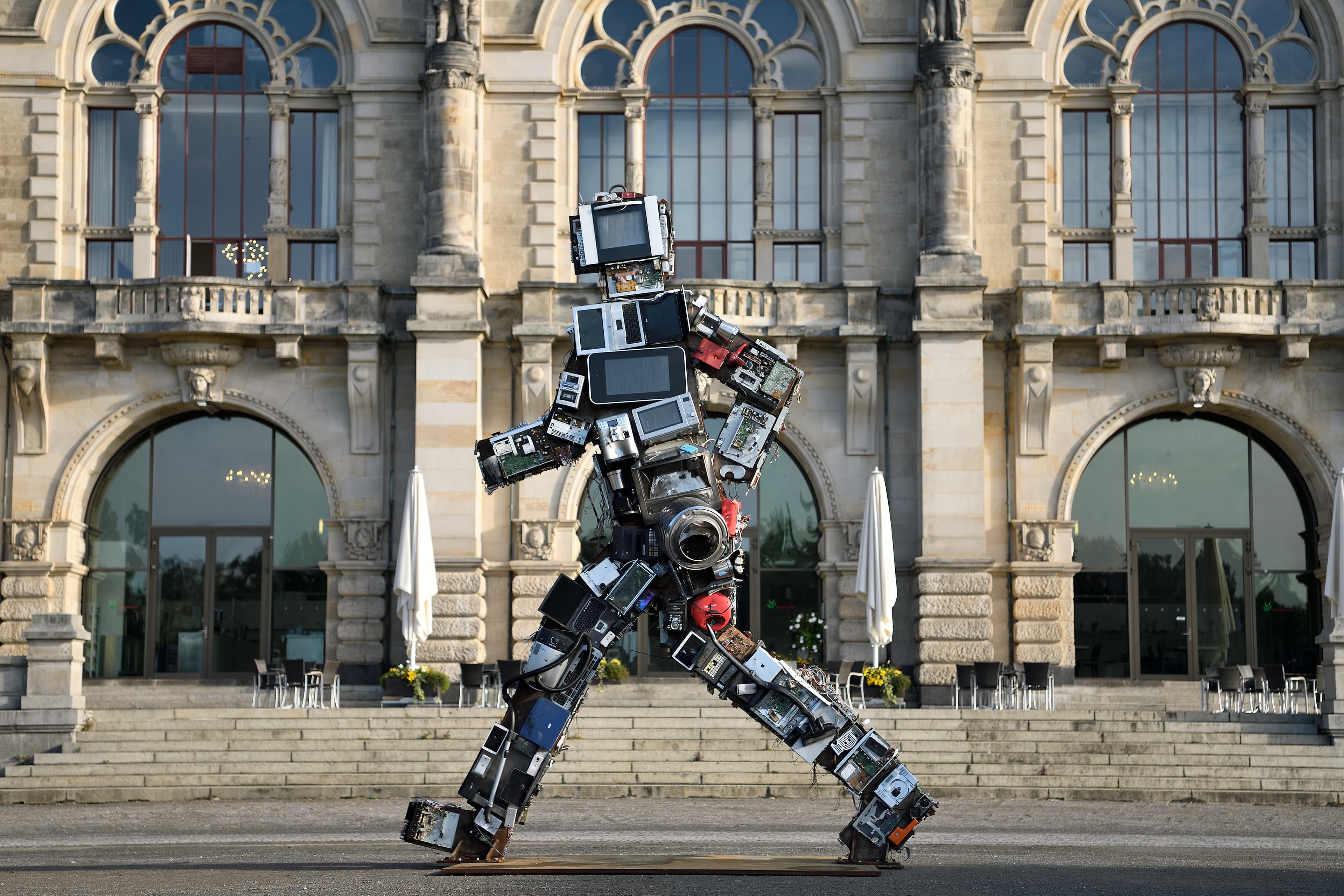 Ein menschenähnliches Kunstwerk aus Elektroschrott steht vor einer Treppe.
