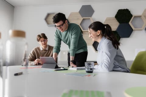 Drei Auszubildene sitzen an einem Tisch und schauen auf ein Tablet.