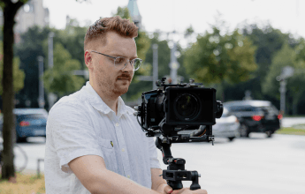 Der Mitarbeiter Julian hält eine Videokamera in der Hand und schaut auf das Display. Im Hintergrund ist eine Straße zu sehen.