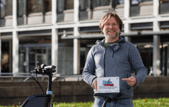 Betriebsratsvorsitzender Peta Hesse steht neben seinem Fahrrad und hält ein Fahrradabzeichen in der Hand.