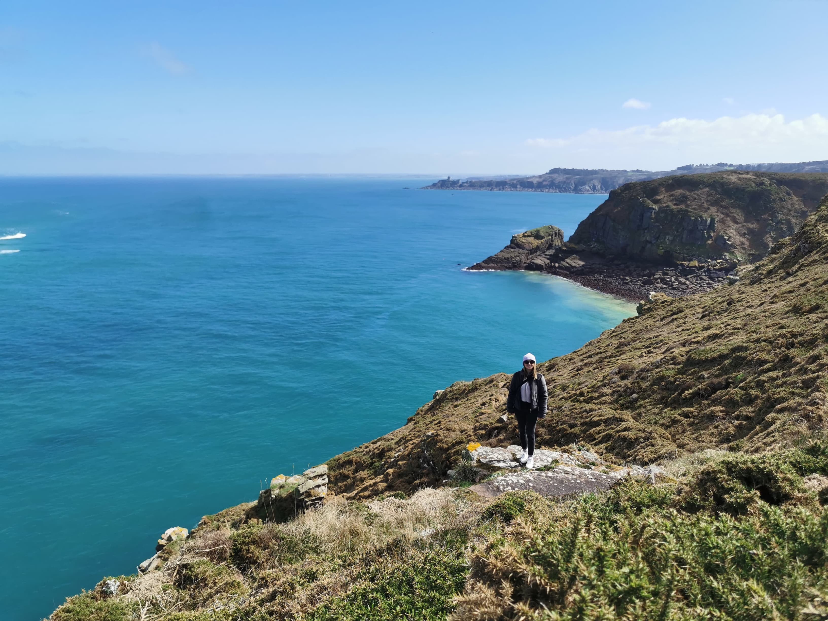 Landschaftaufnahme von einer Steilküste mit Meer. Klein zu erkennen ist die Mitarbeiterin Karina, die dort ihre Workation verbringt.