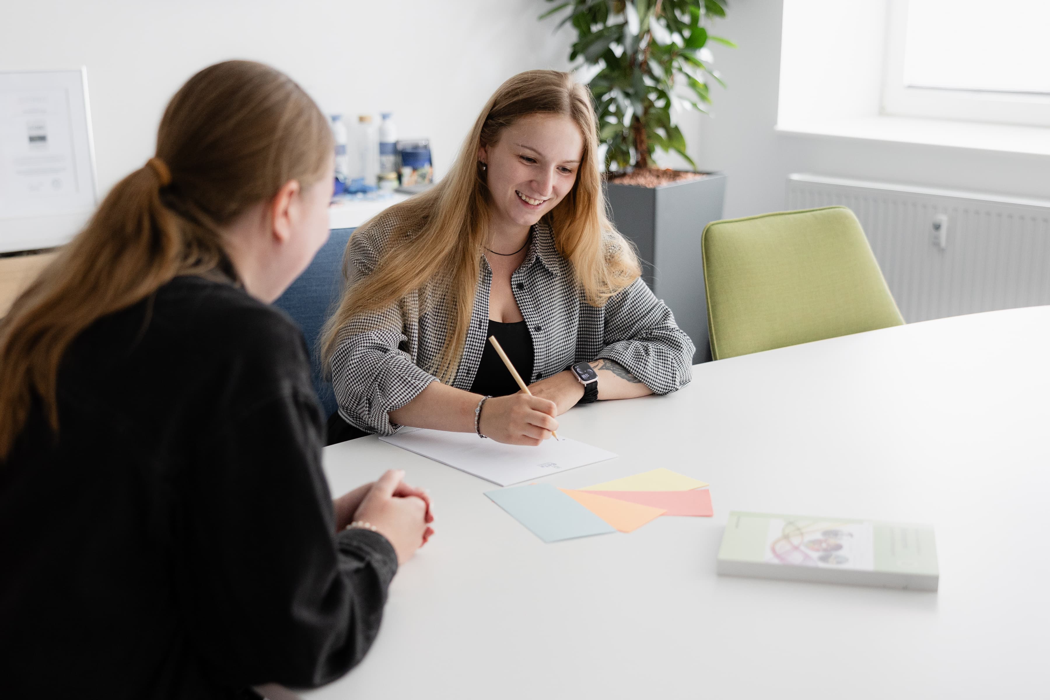 Zwei Auszubildende der WERTGARANTIE Group sitzen während einer JAV-Sitzung an einem Tisch und machen Notizen.
