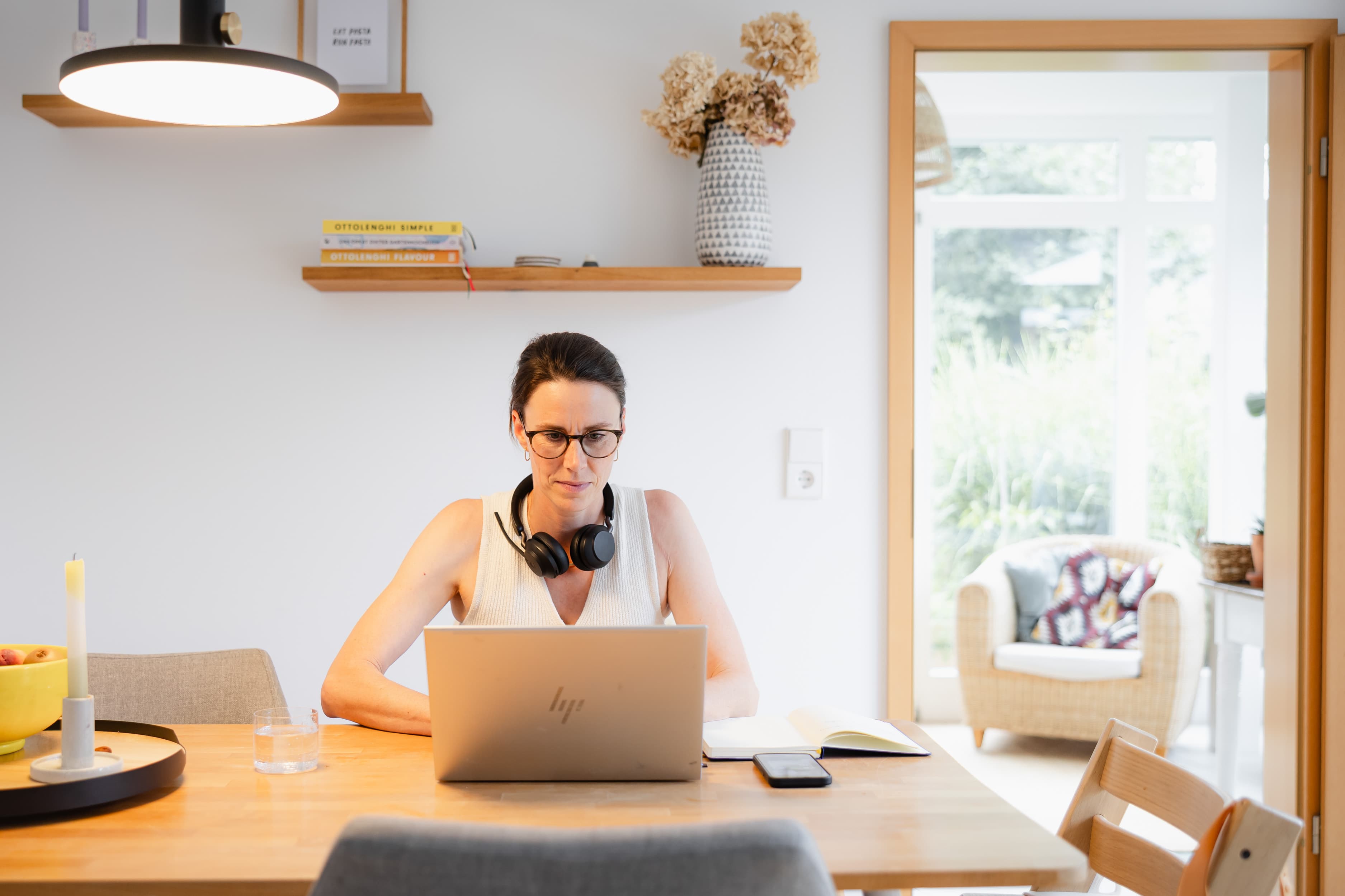Eine Mitarbeiterin der WERTGARANTIE Group sitzt im Homeoffice an ihrem Esstisch mit einem Laptop vor ihr und einem Headset um den Hals.