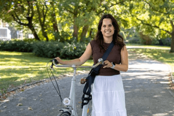 Paula Strufe aus dem HR-Bereich ist im Park unterwegs und hält seitlich ihr Fahrrad fest.